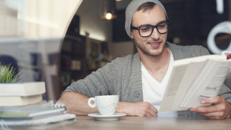 Lächelnder Mann liest Buch im Café