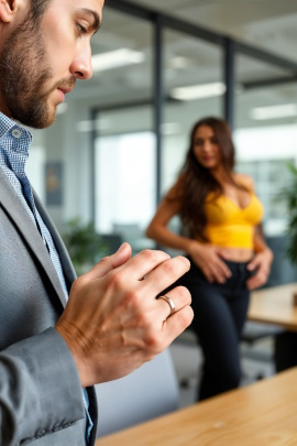 Mann schaut im Büro auf Ehering, während attraktive Kollegin zur Tür hereinkommt