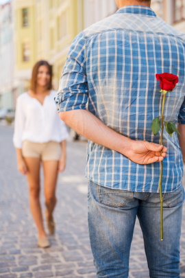 Mann mit Rose hinterm Rücken begrüßt Frau beim Dating