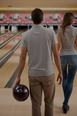 Mann beim Bowlingwurf von hinten mit attraktiver Frau daneben