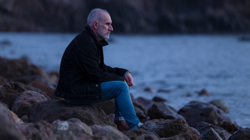 Mann in Midlife Crisis sitzt am Fluss und denkt über sein Leben nach