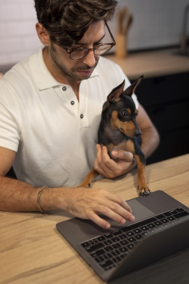 Mann mit Hund sitzt zu Hause am Tisch und tippt am Laptop