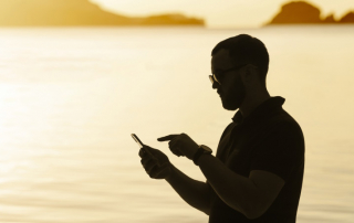 Mann im Schatten am Meer schaut aufs Handy