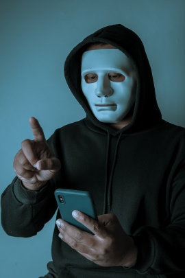 Maskierter Mann schaut mit erhobenem Zeigefinger aufs Handy
